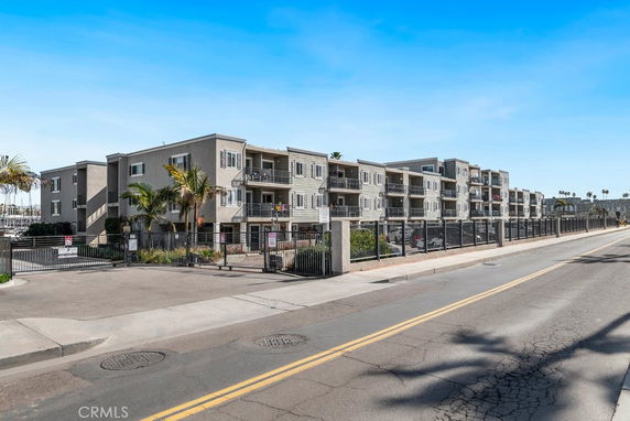 Front view of a multi-story apartment complex with balconies and gated entrance.