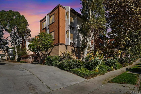 Front view of a multi-story building with a driveway and surrounding trees.