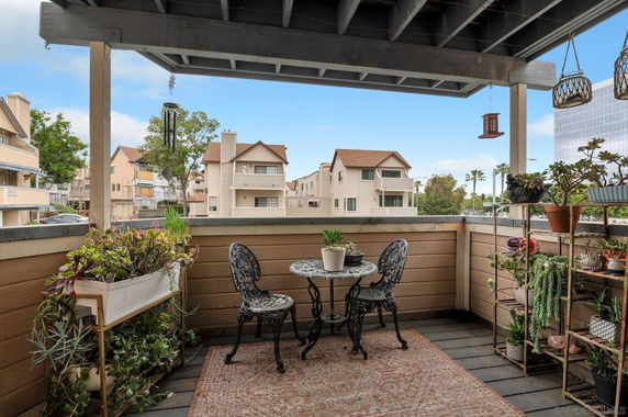 View from a balcony with potted plants and outdoor furniture, showing neighboring residential buildings.