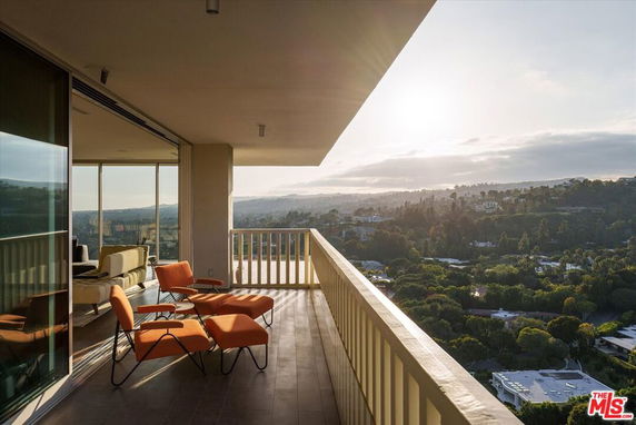 Balcony with orange lounge chairs overlooking a scenic landscape with hills and trees.