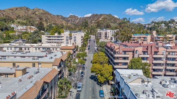 Aerial view of a street lined with residential buildings and surrounded by hills.