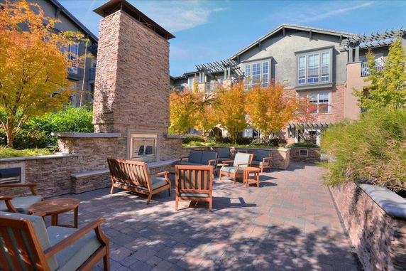 Outdoor seating area with brick fireplace and surrounding buildings.