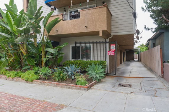 Front view of a multi-story building with a covered parking area and surrounding plants.