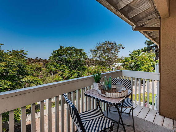 Balcony view with outdoor furniture overlooking trees and a road.