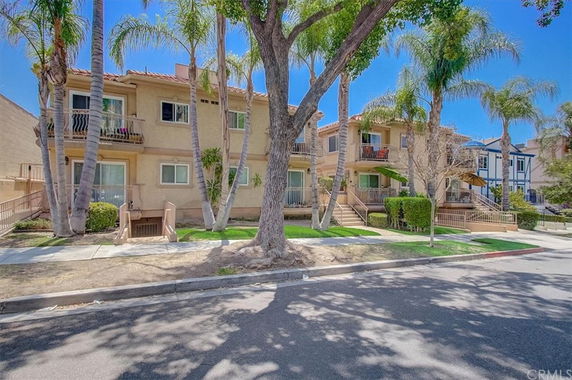 Front view of a two-story apartment building with balconies and palm trees in front.
