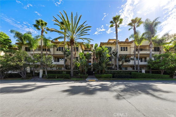 Front view of a multi-story building with balconies, surrounded by tall palm trees.