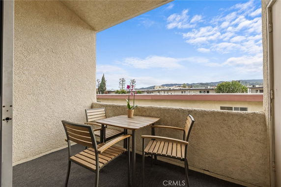 Balcony view with outdoor seating overlooking rooftops and distant hills.