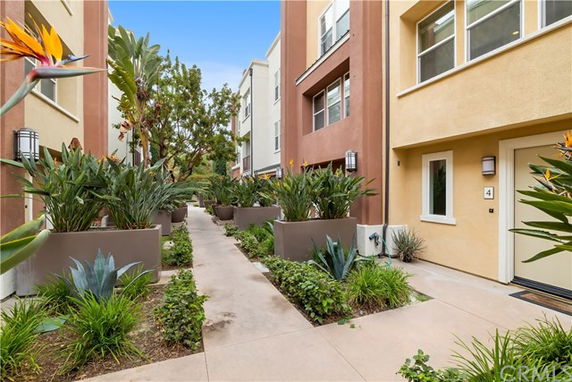 Pathway between multi-story residential buildings with planters and greenery.