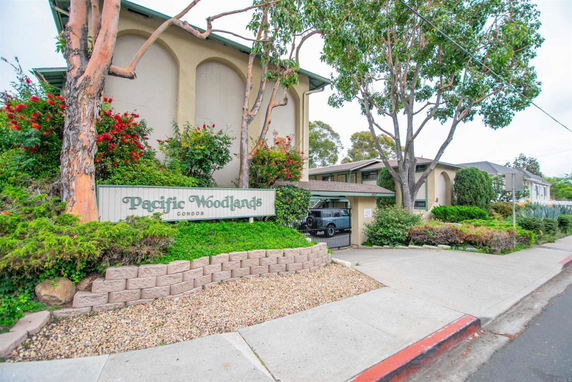 Front view of a multi-story condo building with a garden and sign reading 'Pacific Woodlands Condos'.