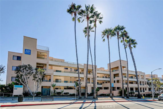 Front view of a multi-story apartment building with balconies and palm trees in front.