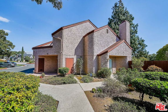 Front view of a multi-story house with a stucco exterior and peaked roof.