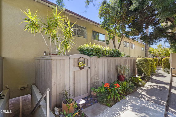 Exterior view of a multi-story residential building with a wooden fence and plants.