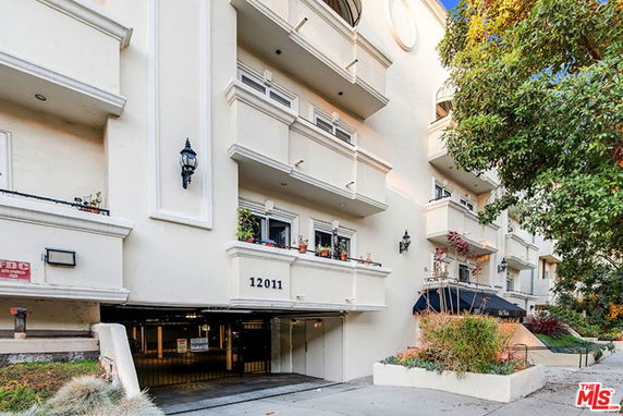 Front view of a multi-story apartment building with balconies and an entrance driveway.