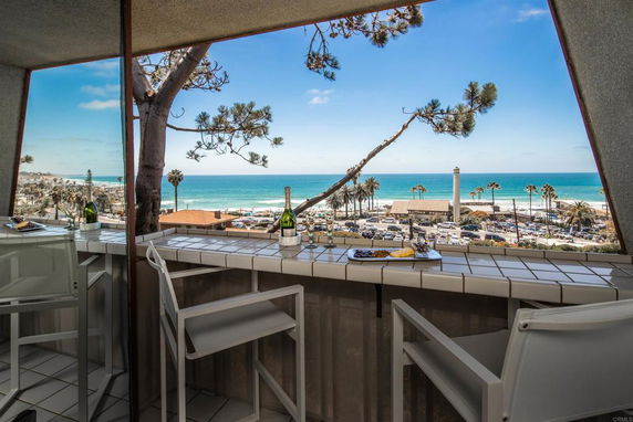 Panoramic view from a balcony overlooking the ocean and surrounding area with seating and a table.