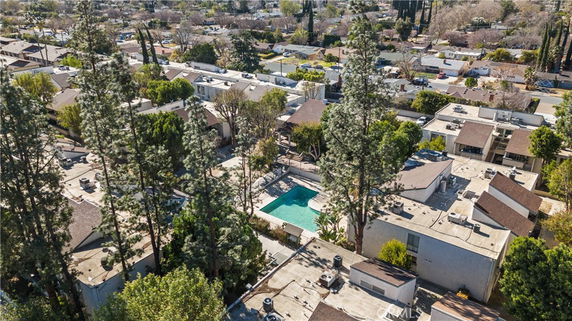 Aerial view of a residential area with multiple houses and a central swimming pool surrounded by trees.