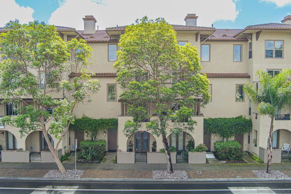 Front view of a multi-story residential building with arched entrances and surrounding trees.