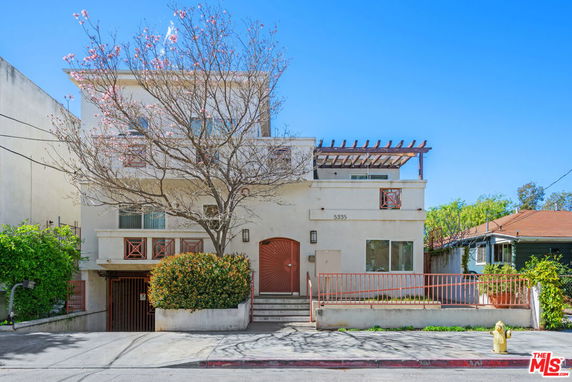 Front view of a multi-story house with balconies and a wooden pergola.