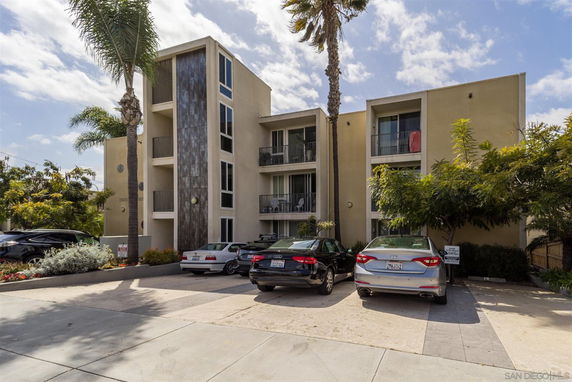 Front view of a three-story apartment building with balconies and parking area.