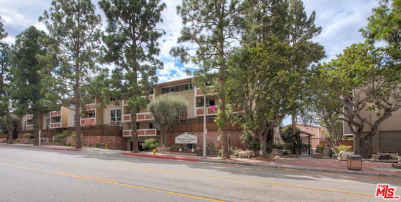 Front view of a multi-story residential building with trees along the road.