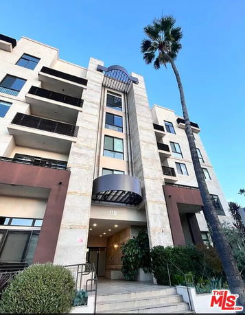 Front view of a multi-story apartment building with balconies and large windows.