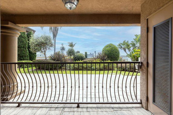 View from a covered patio area towards a garden with various plants and distant buildings.