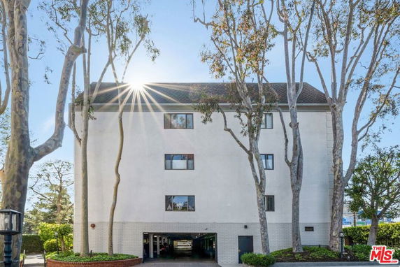 Front view of a multi-story building with trees and sunlight.