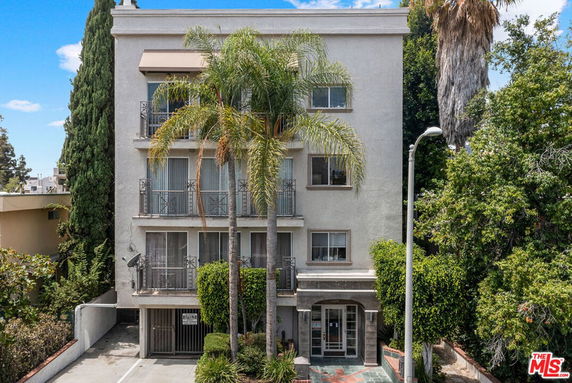 Front view of a multi-story apartment building with balconies and palm trees in front.