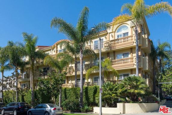 Front view of a multi-story apartment building with balconies and palm trees.