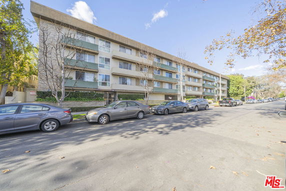 Front view of a multi-story apartment building with parked cars along the street.