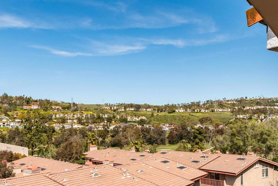 Panoramic view of a neighborhood with multiple houses and green hills in the background under a blue sky.