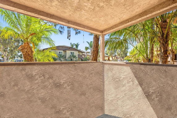 View from a covered outdoor area with plaster walls, looking towards trees and residential buildings.