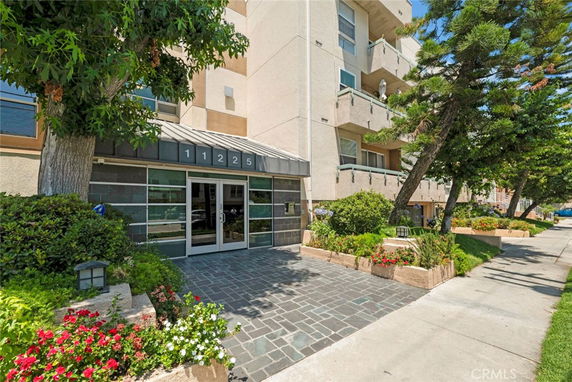 Front view of a multi-story building with balconies and entrance area with a tiled path.