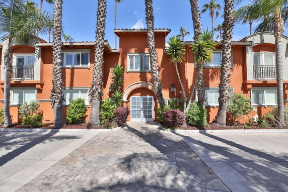 Front view of a two-story house with arched doorway and palm trees.