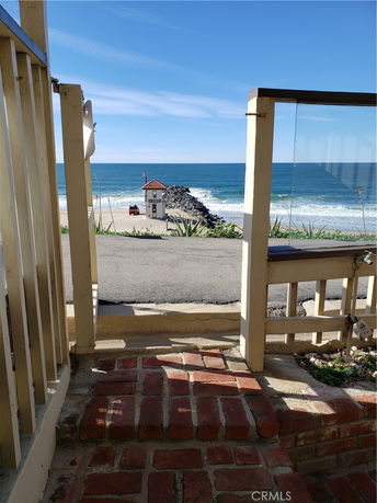 View from a building looking out to the ocean with sandy beach and a small structure on a rocky jetty.