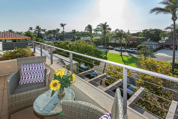 Balcony view overlooking a street with palm trees and buildings in the distance.