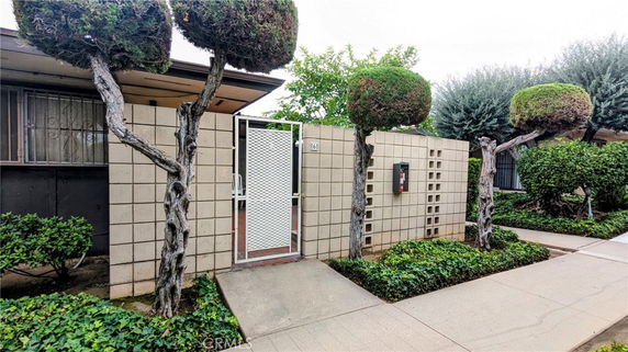 Front view of a house with a brick wall and metal gate, surrounded by manicured shrubs and trees.