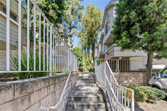 Front view of a multi-story apartment building with a stairway leading up surrounded by trees and a railing.