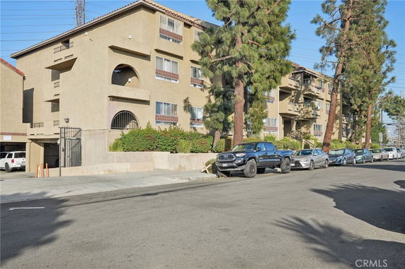 Front view of a multi-story apartment building with trees and parked cars.