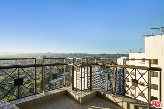 Balcony view from a high-rise building overlooking cityscape and distant hills.