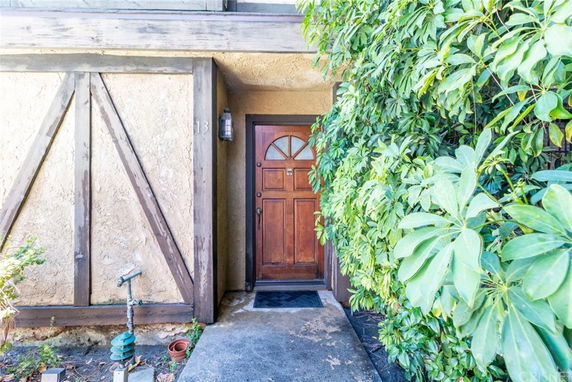 Front view of a house entry with a wooden door and number 13 next to it, surrounded by greenery.