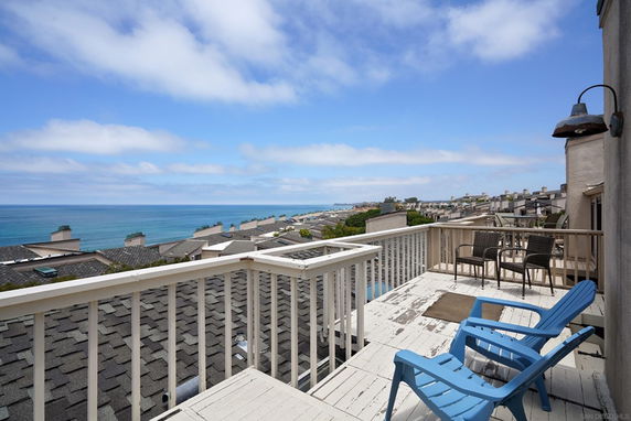 View from a rooftop deck overlooking the sea and neighboring rooftops with seating area.
