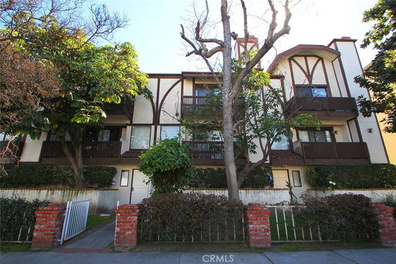 Front view of a three-story apartment building with wooden balconies and a gabled roof.