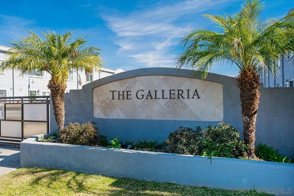 Front view of a building entrance with a sign reading 'The Galleria' flanked by palm trees.