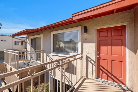 Front view of a two-story building with external walkway and red door.