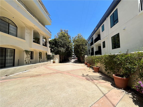 Front view of multi-story residential buildings with balconies and potted plants along the pathway.