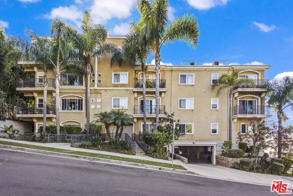 Front view of a multi-story residential building with balconies and palm trees.