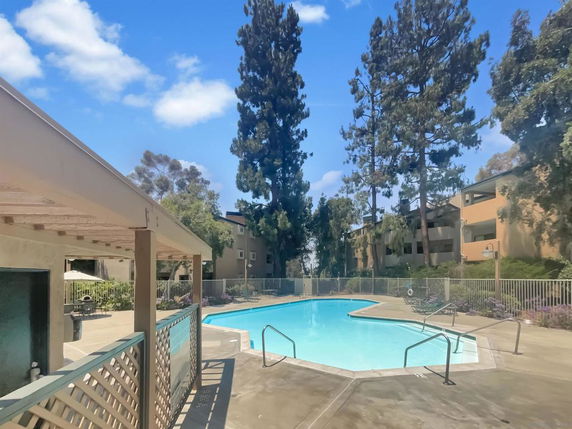 Outdoor swimming pool area with buildings and trees in the background.