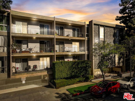 Front view of an apartment building with balconies and a parking area in the foreground.