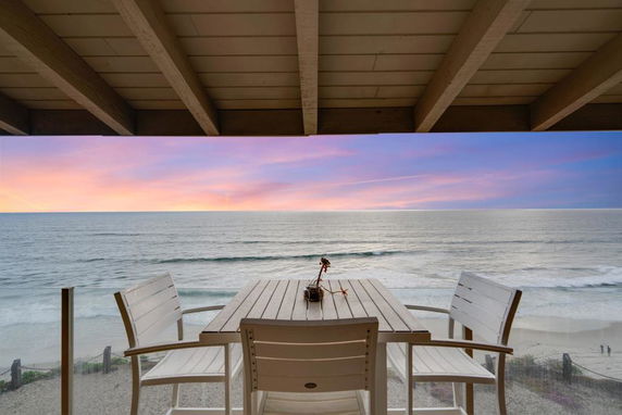 Outdoor view from a terrace overlooking the ocean with a table and chairs.