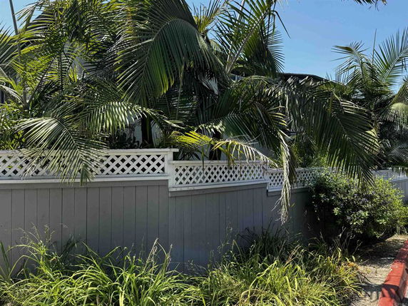 Plants and palm trees next to a decorative fence outside a building.